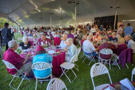 A large group of alumni are seated at round tables under the tent at Reunion.