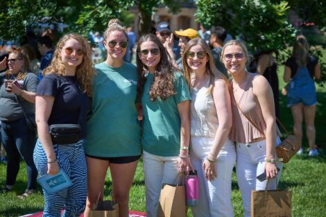 A group of five alumnae are standing on the Quad and smiling at the camera.