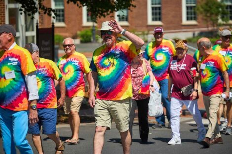 A group of alumni are walking in the parade. They are wearing tie-dye t-shirts.