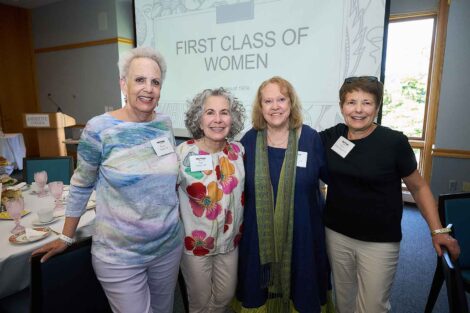 A group of four alumnae are standing together looking at the camera.