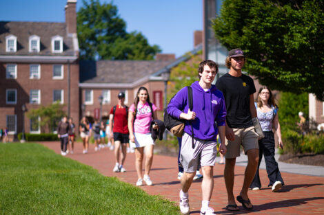 Students smile, walking across a brick path of campus.