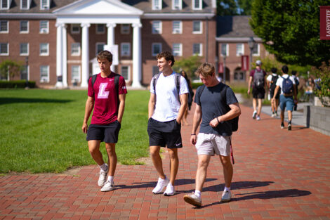 Three students smile, walking across a brick path of campus.