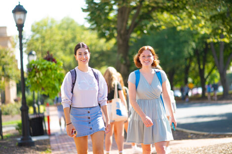 Two students smile, walking across a brick path of campus.