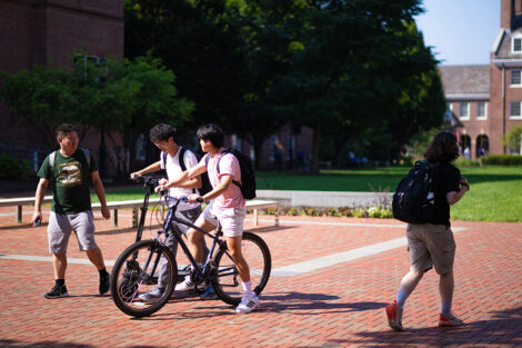 Two students chat with another student while getting on to their bikes.