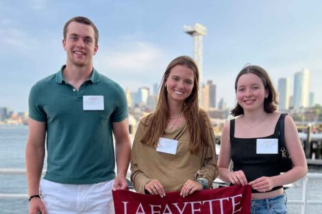 Incoming members of the Class of 2028 from Boston are smiling at the camera. They are holding a Lafayette flag.