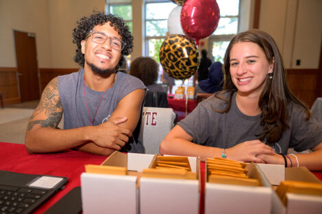 Two students smile as they check in arriving students.