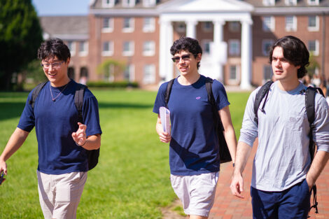 Three students walk across a brick path.