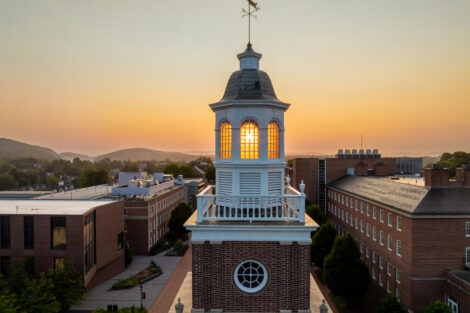 The sun shines through windows on top of a building cupola at sunrise.