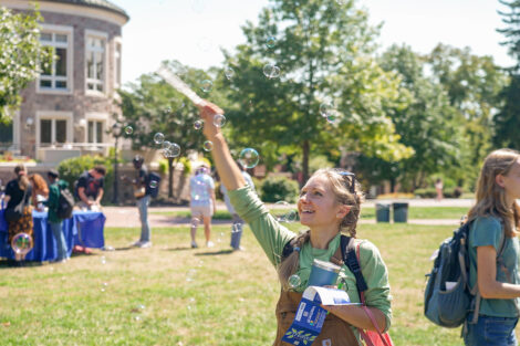 A student uses a bubble wand on the Quad, smiling