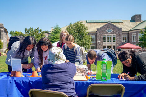 Students write on pieces of paper at a long table.