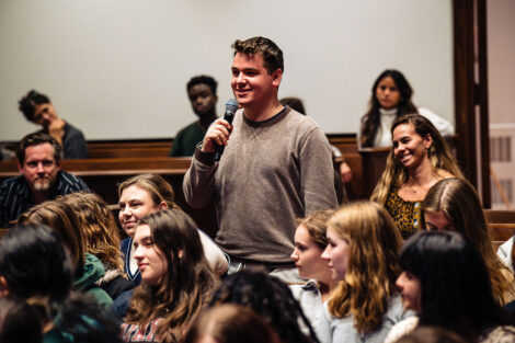 A student in a crowd stands up with a microphone to ask Daveed Diggs a question.