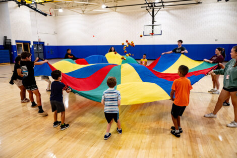 Lafayette students and elementary students play with a parachute in a gymnasium.