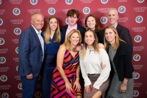 Eight family members stand in front of a Lafayette College maroon backdrop. They are smiling at the camera.