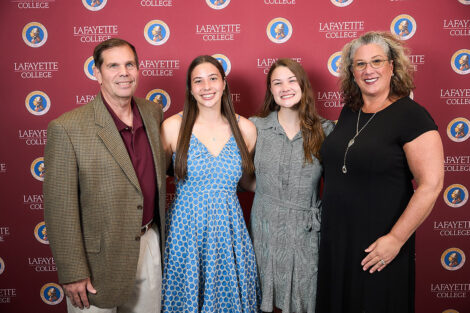 Four family members stand in front of a Lafayette College maroon backdrop. They are smiling at the camera.