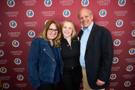 Three family members stand in front of a Lafayette College maroon backdrop. They are smiling at the camera.