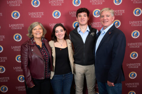 Four family members stand in front of a Lafayette College maroon backdrop. They are smiling at the camera.