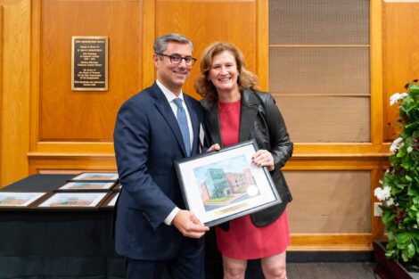 Sebastian “Benny” Crapanzano ’97, P’26 is standing with President Nicole Hurd. They are holding a framed photo.