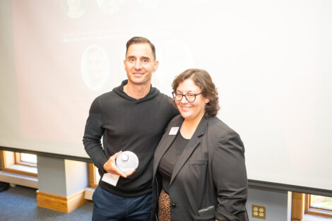 Mark Suffredini ’93 is standing with Alexis Leon. Mark is holding a glass award.