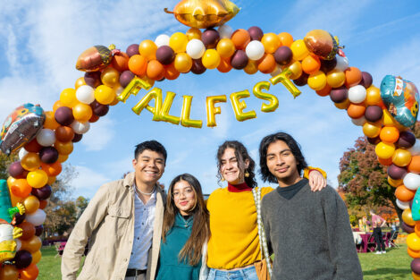 A family of four are standing underneath a balloon arch that read fall fest.