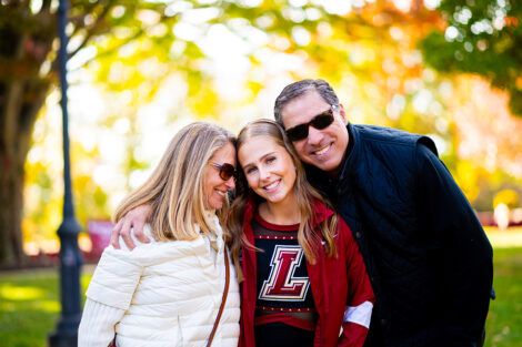 A mom and dad hug their student. The student is wearing a cheerleading uniform.