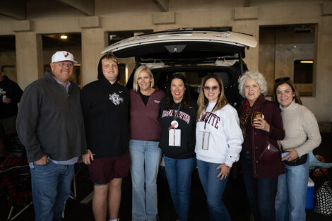 A group of seven are tailgating before the football game. They are wearing lafayette shirts.