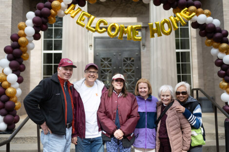 A group of six stand under a Welcome Home banner.