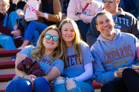 A family of three is sitting in the stands at a football game.