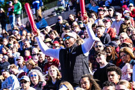 A fan is standing in the crowd and waving two maroon plastic goal posts