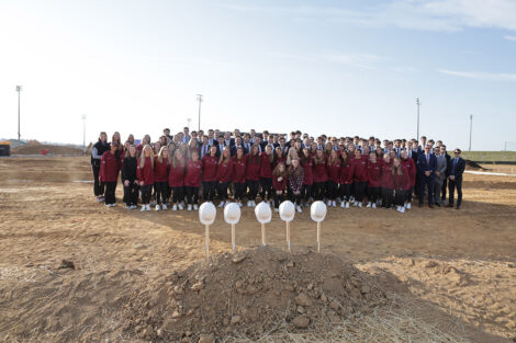 Wide shot of the men's and women's lacrosse teams with hard hats and shovels in the foreground.