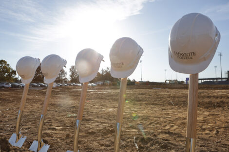 Five shovels are in the ground with white hard hats on the top of each handle