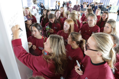 A group of female student athletes are in line to sign a beam