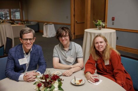 Three family members are seated at a table. They are smiling at the camera.