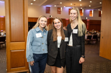 Caillin Burke '26, Madden Murray '28, and Rachel Lange '28 are standing arm in arm and smiling at the camera.