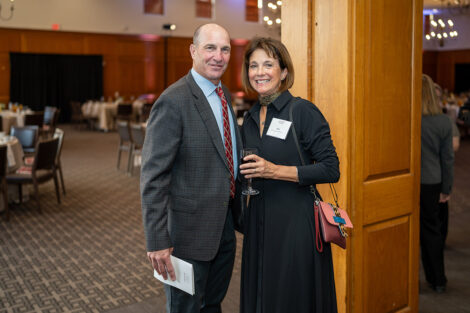 Bill and Barbara Tucker '81 P'08 '11 are standing next to each other and smiling at the camera. Barbara is holding a glass.