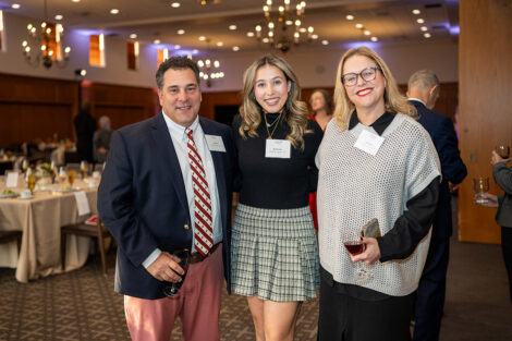 Two parents are standing with their daughter at the Marquis Founders Dinner. They are smiling at the camera.