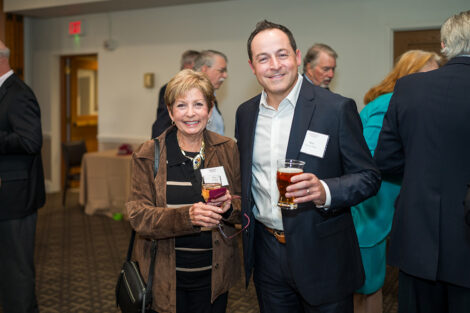 Two alumni are standing next to each other at the Marquis Founders Dinner. They are smiling at the camera and holding drinks.