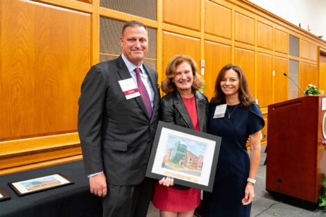 Peter S. Ruggiero P’20,’25 and Liselle M. Ruggiero P’20,’25 are standing with President Nicole Hurd (center). Hurd is holding a framed photo.