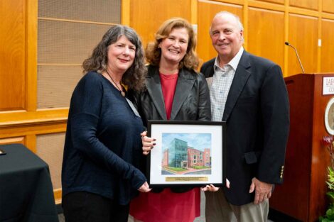 Linda Checchio McCarron Esq. '86, P'28 and Edward McCarron P'28 are standing with President Nicole Hurd. They are holding a framed photo.