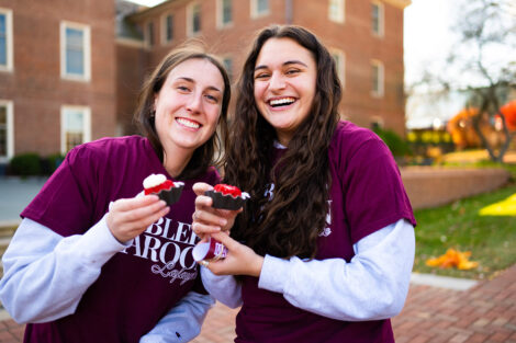 Two students smile, holding cupcakes.