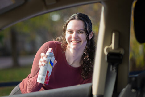 A student smiles spray painting a car.