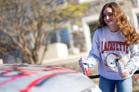 A student smiles spray painting a car.