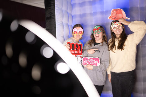 Students smile, holding props, in a photo booth.