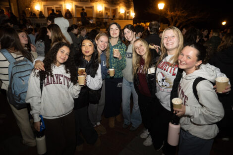 Students stand and smile with hot chocolate.