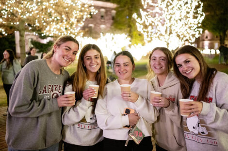 Students stand and smile with hot chocolate.