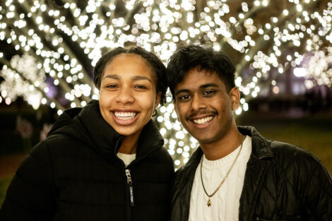 Two students smile in front of lit up trees.