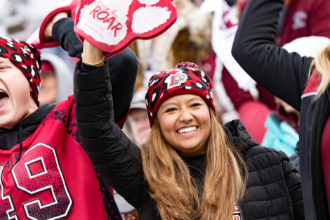 A student smiles in the crowd with a Bring the Roar foam finger.