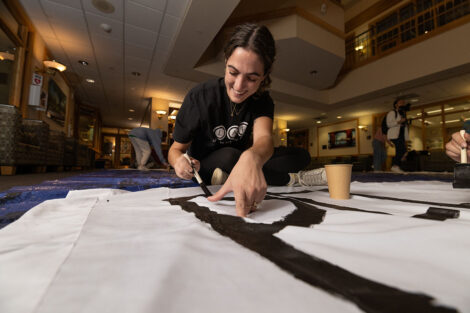 A student paints words onto a white bedsheet.