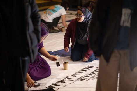 A student paints words onto a white bedsheet.