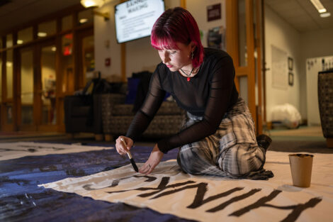 A student paints words onto a white bedsheet.