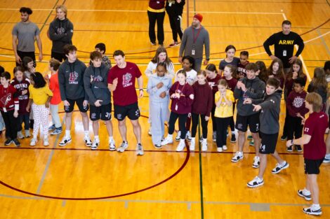 Teachers, students, and men's lacrosse players line up on the basketball court.